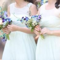 Two women in white dresses holding small blue-and-green bouquets at a wedding ceremony