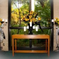 Floral arrangement with sunflowers and candles on a wooden console table before a window.