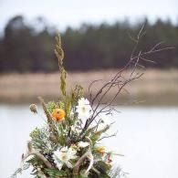 Wildflower bouquet with white and orange blossoms by a calm lake, trees blurred in the background