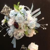 White and pale blue floral bouquet with ribbons and bead accents on a dark background