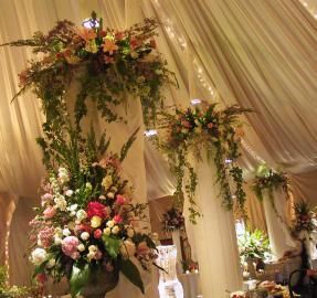 Flower-covered wedding arch and columns draped in cream fabric, with soft lighting and floral arrangements.