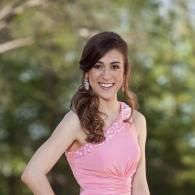 Smiling woman in a pink dress standing outdoors with a blurred green background