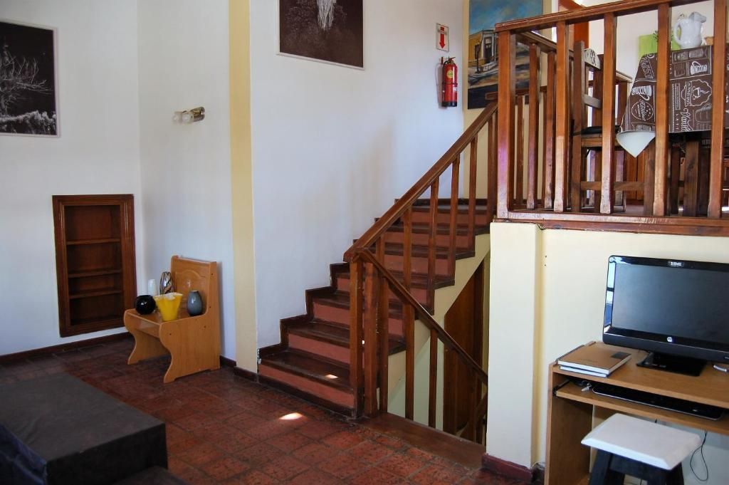 Escalera con barandilla de madera en una sala de estar, con un televisor sobre un pequeño soporte y una alfombra oscura en el suelo.
