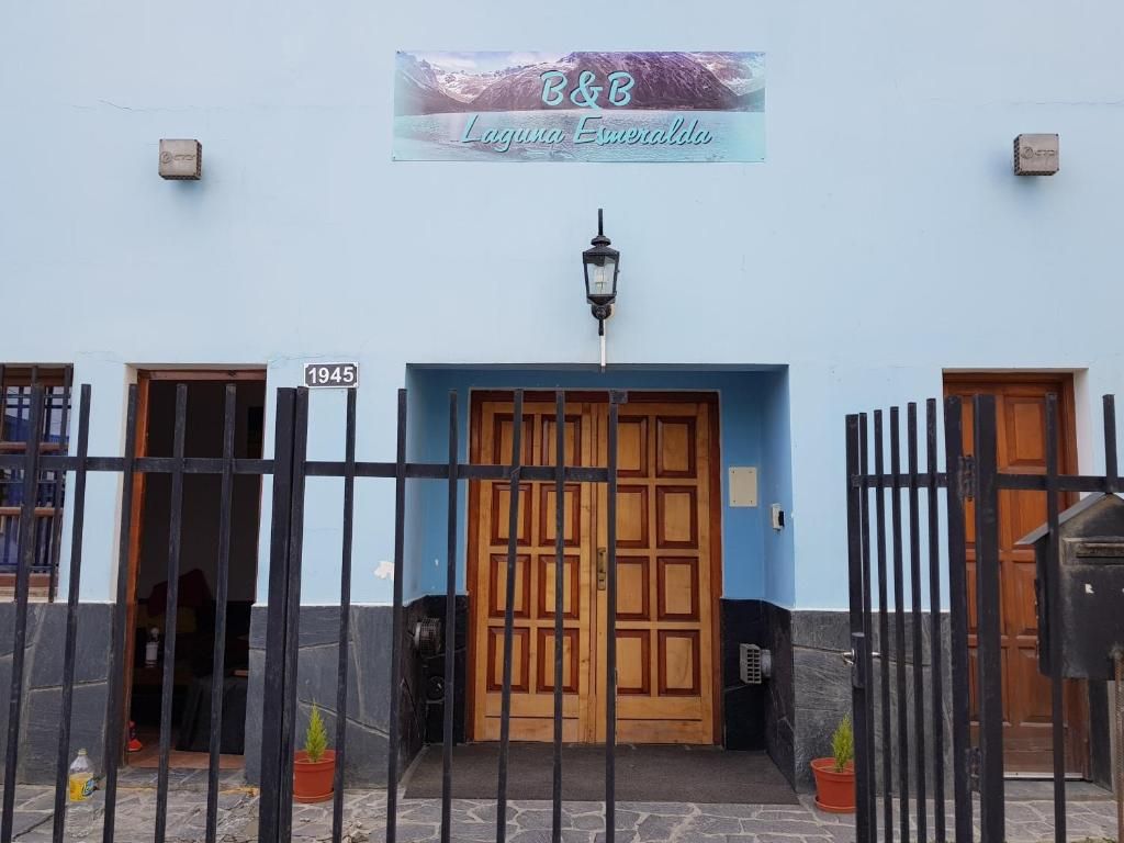 Vista frontal de un edificio blanco con una puerta doble de madera, una verja de hierro y un letrero sobre la entrada.