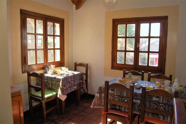 Acogedor comedor con mesas y sillas de madera junto a dos ventanas que reciben una cálida luz del sol.