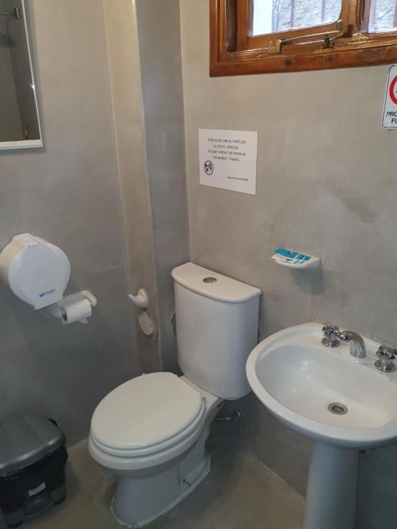 Baño pequeño con inodoro, lavabo, dispensador de papel higiénico y ventana.