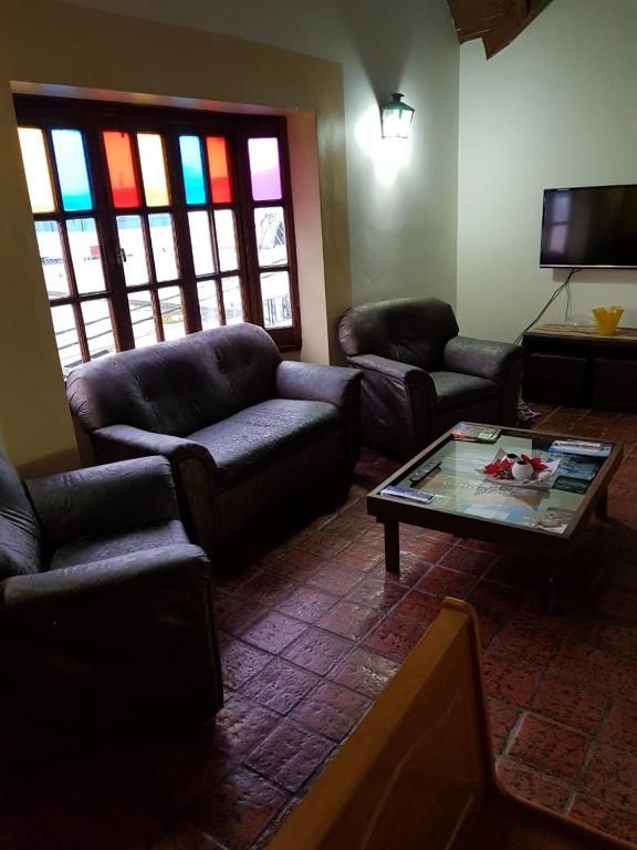 Pequeña sala de estar con sofás, mesa de centro, televisor de pared y una ventana colorida.