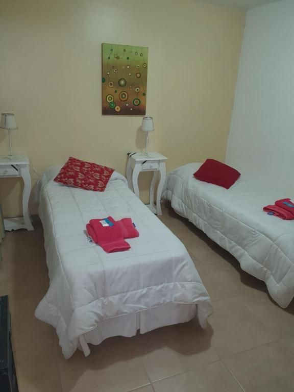 Habitación pequeña con dos camas individuales, sábanas blancas, almohadas rojas y mesitas de noche.