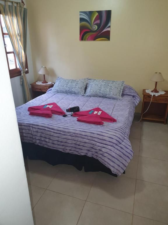 Cama bien hecha con edredón a rayas, toallas rojas y lámparas de noche en un dormitorio luminoso.