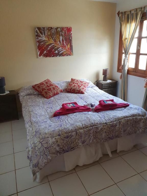 Habitación con una cama vestida con ropa de cama estampada con flores, toallas rojas, mesitas de noche y luz natural que entra por la ventana.