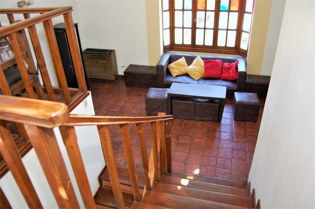Escalera con vistas a una pequeña sala de estar con un sofá, cojines coloridos y suelo de baldosas.