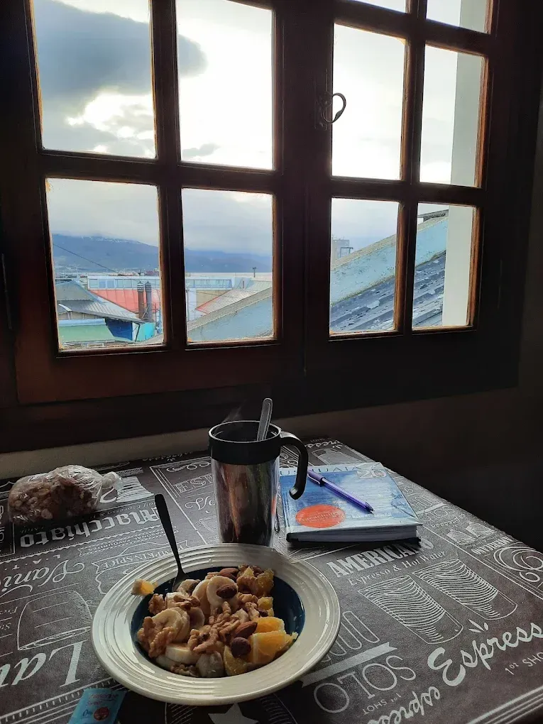 Desayuno en una mesa junto a una ventana con vistas a las montañas y los tejados.