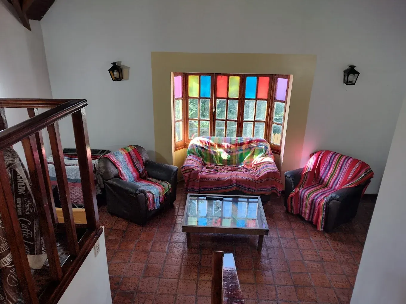 Acogedora sala de estar con ventana colorida, sillones a rayas, sofá y una pequeña mesa de centro de madera.