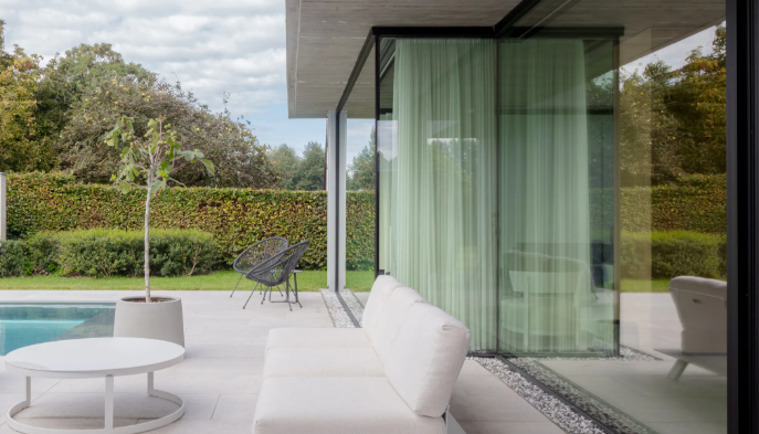 Terras met zwembad, witte bank, tafel, glazen wanden en uitzicht op het groen.