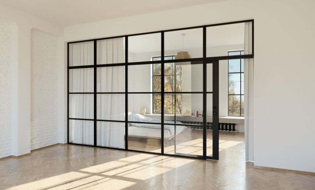 Moderne kamer met een zwarte glazen wand die twee ruimtes scheidt, waarvan één met een bed, gordijnen en natuurlijk licht.