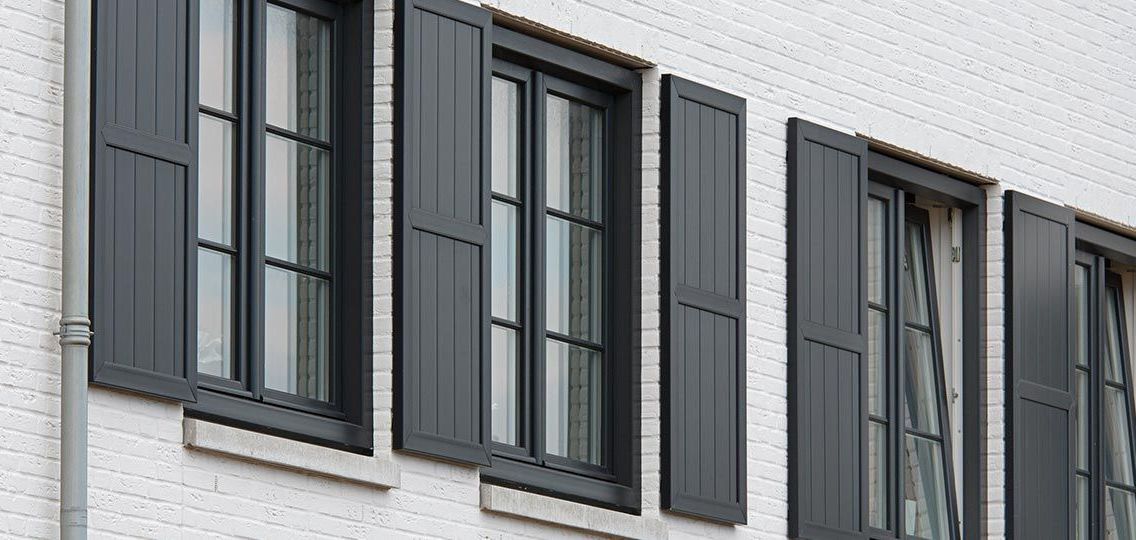 Een wit bakstenen gebouw met zwarte luiken voor de ramen.