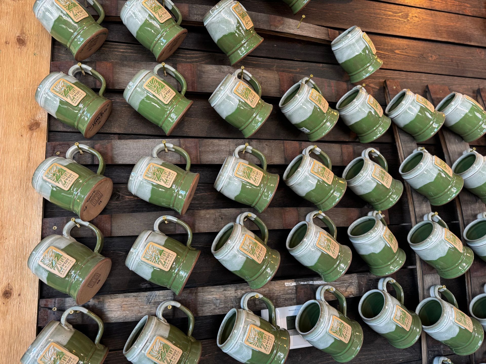 A row of green and white mugs hanging on a wooden wall.
