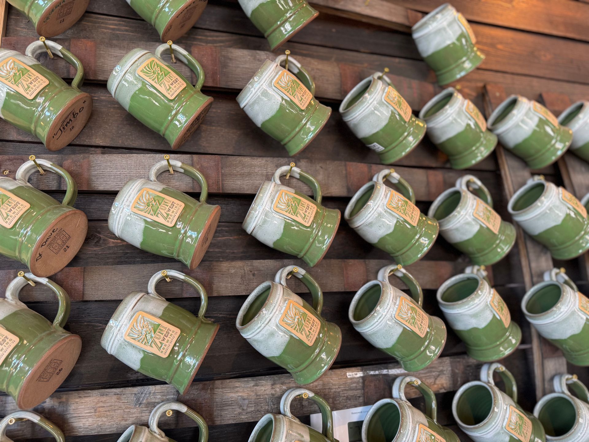 A row of green and white mugs hanging on a wooden wall.