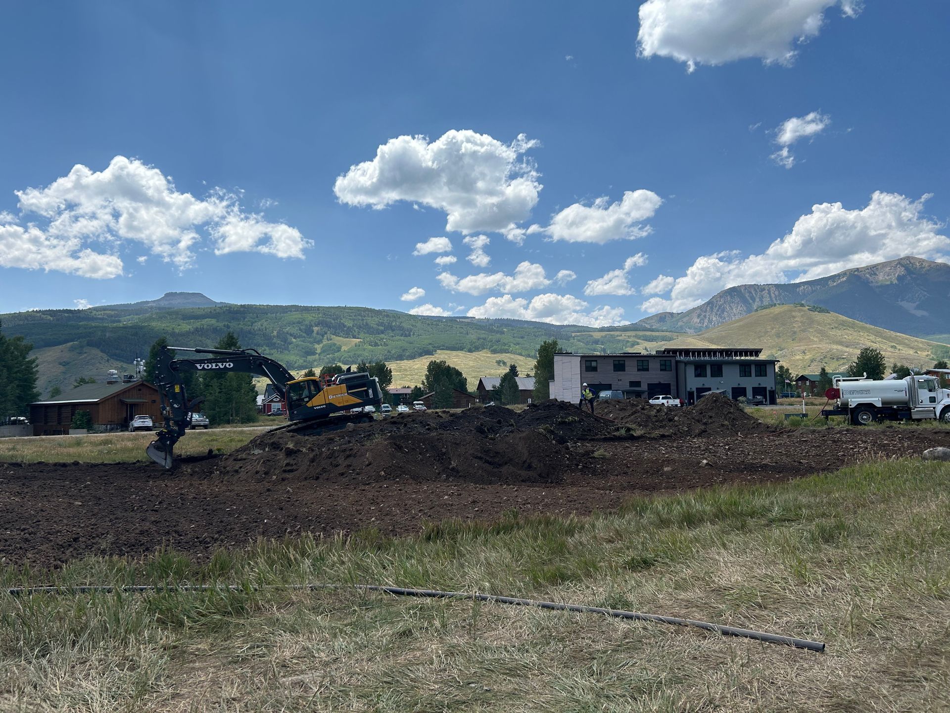 A large pile of dirt is being excavated in a field with mountains in the background.