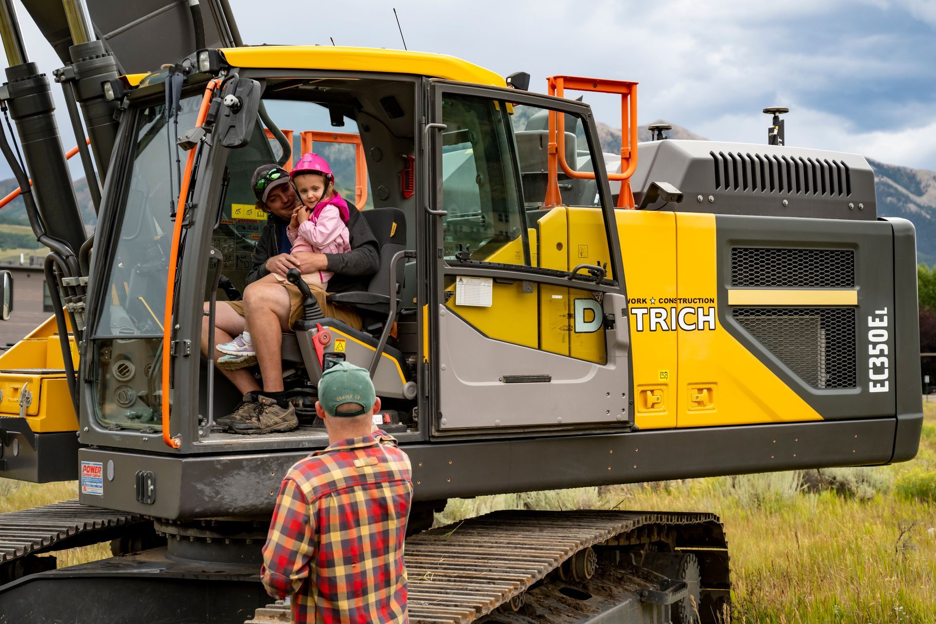 A man and a child are sitting in a yellow excavator.