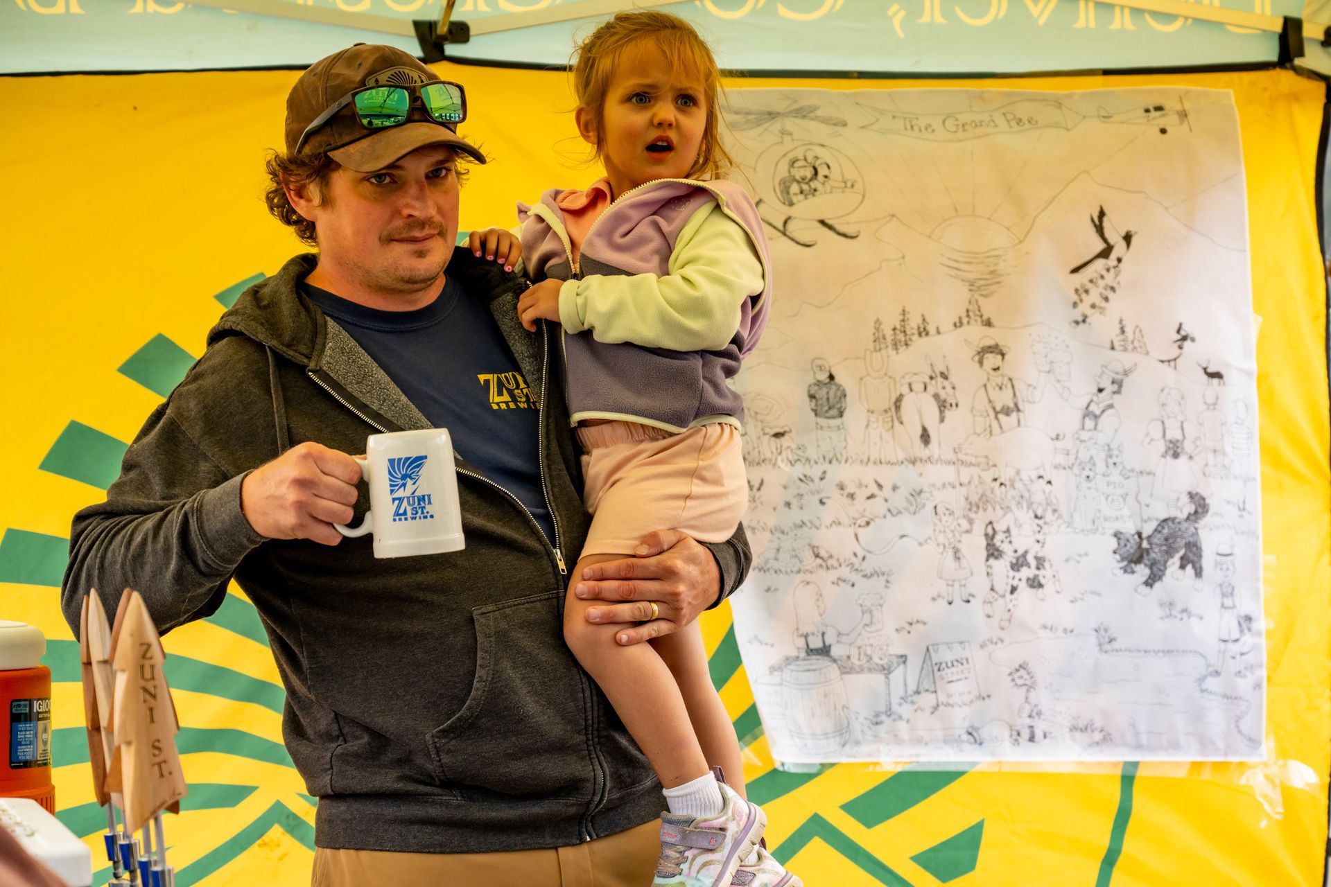 A man is holding a little girl in his arms while holding a mug.