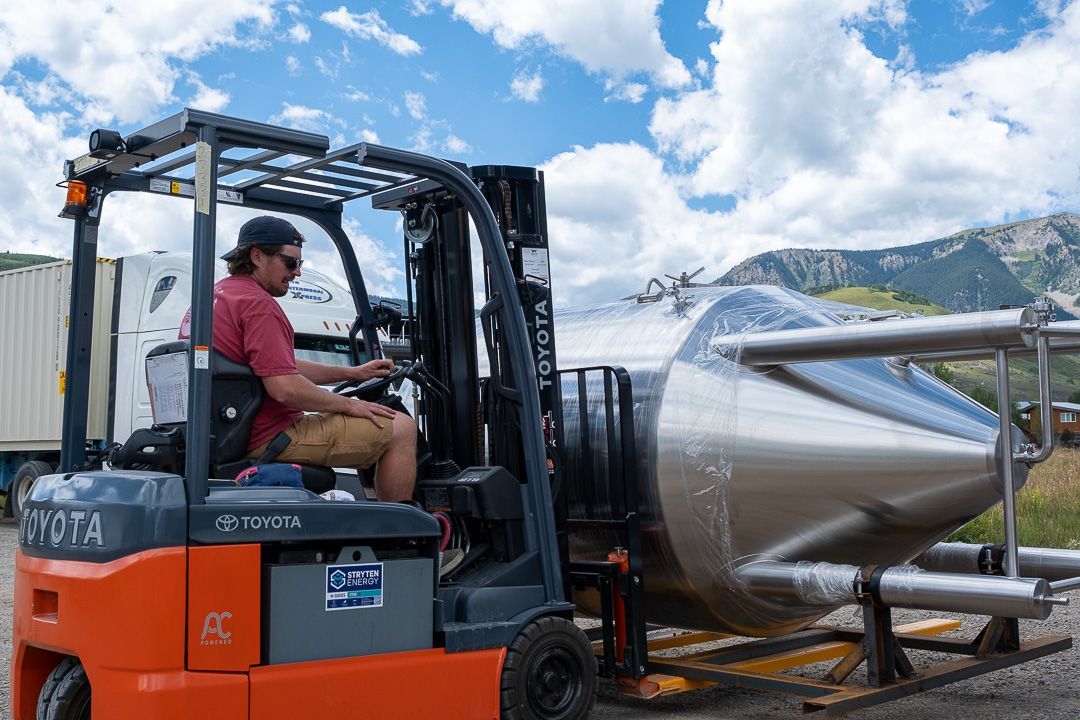 A man is driving a forklift next to a large metal object.