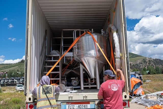 Two men are loading a large tank into a shipping container.