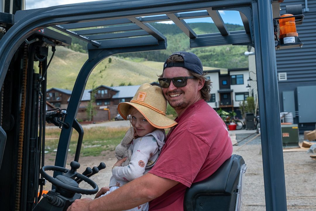 A man is holding a baby while driving a forklift.