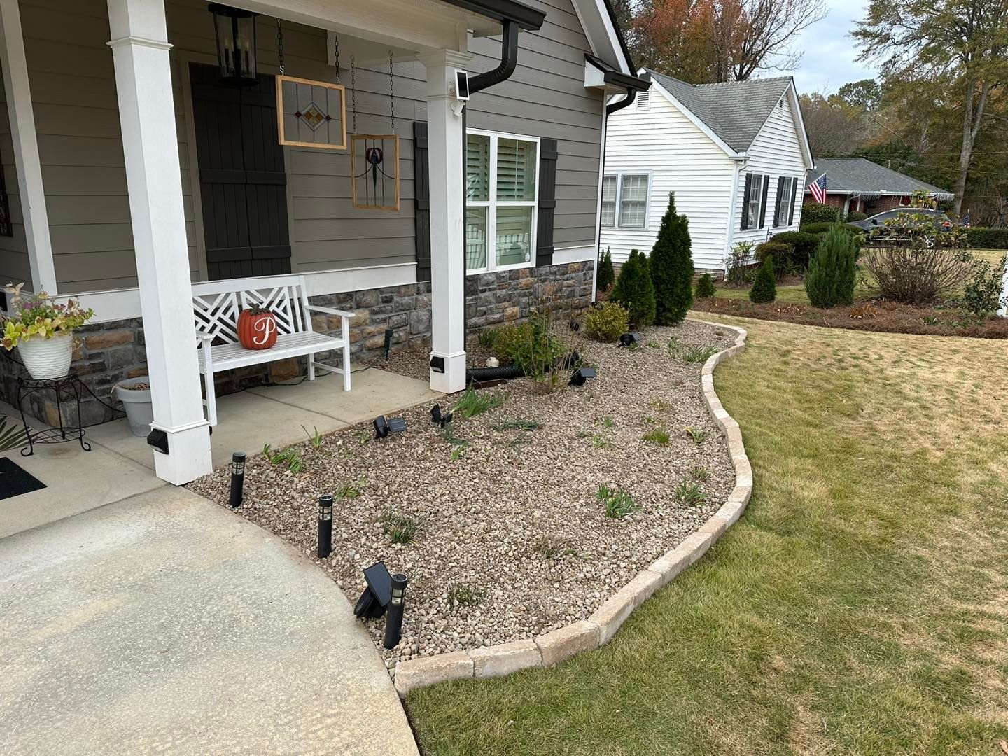 A gray-sided house exterior featuring a front porch with a white bench, a rock landscaping bed, and exterior lighting.