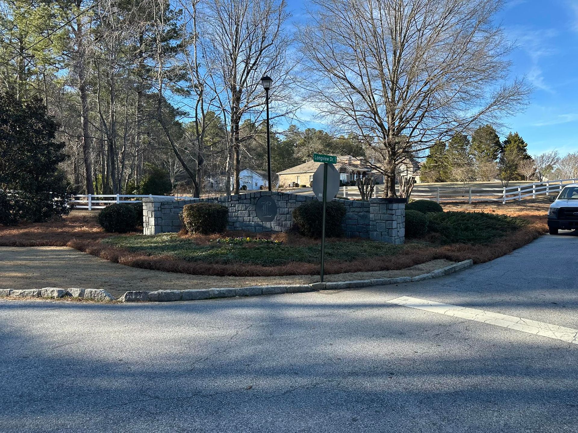 A stone entrance monument for a residential community under a bright blue sky, surrounded by trees and a white fence.