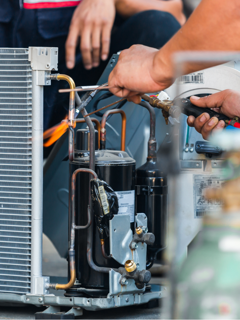 Technician using a torch to repair a metal appliance, with orange flames and exposed wiring.