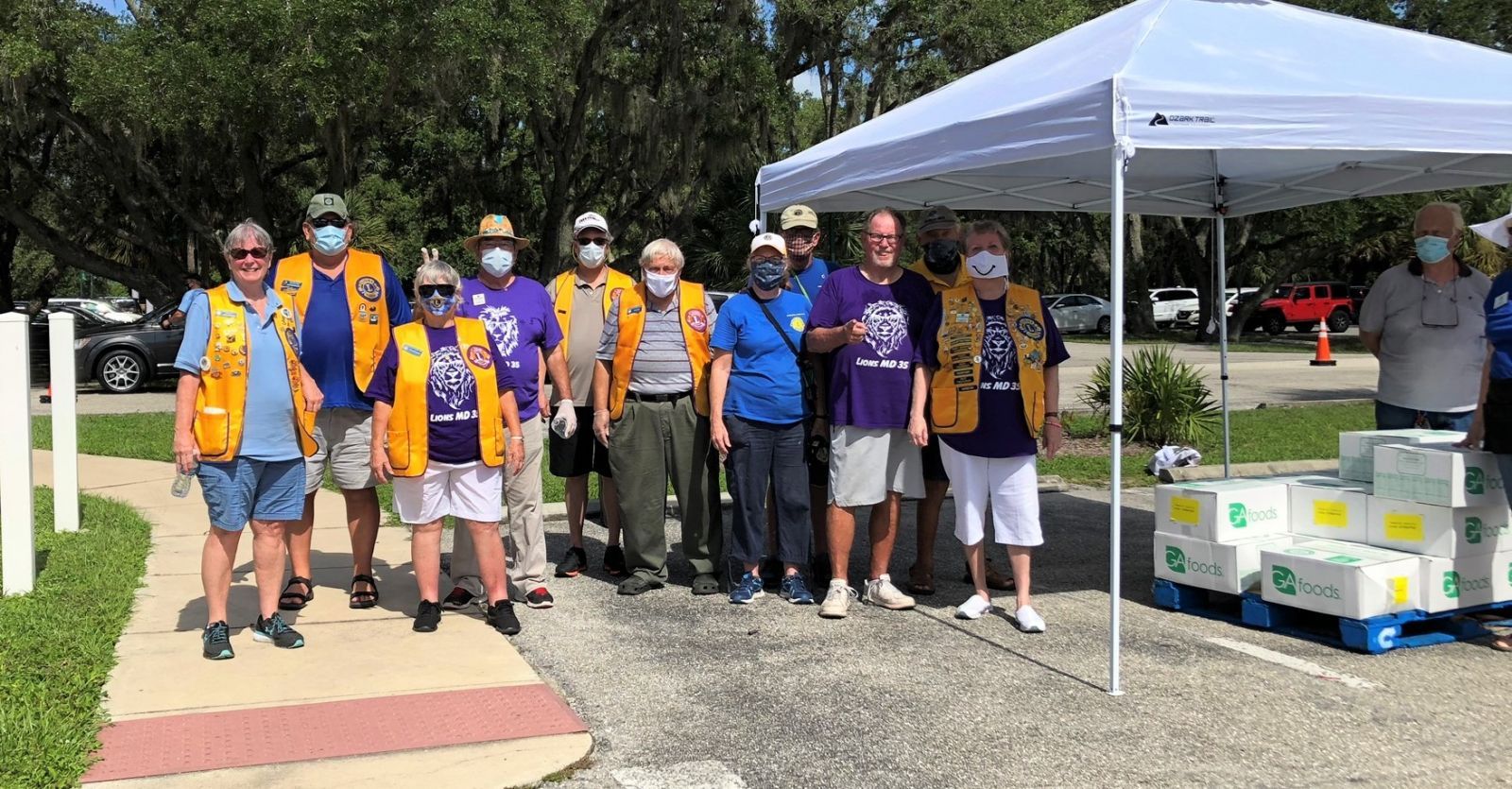 A group of people are standing under a tent in a parking lot.