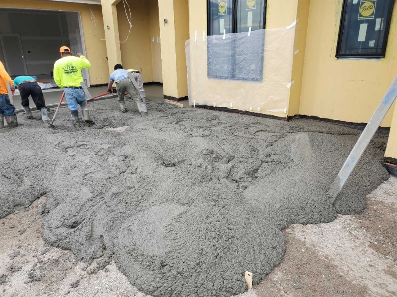 A group of men are working on a concrete driveway in front of a house.