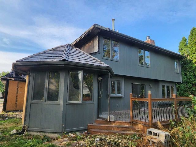 A large gray house with a wooden deck and stairs in front of it.
