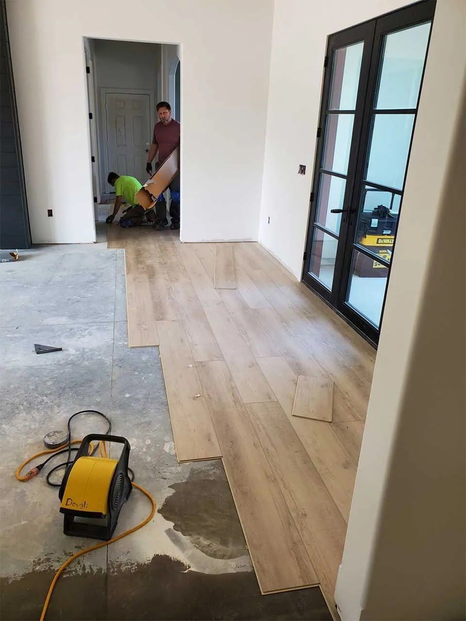 A couple of men are working on a wooden floor in a room.
