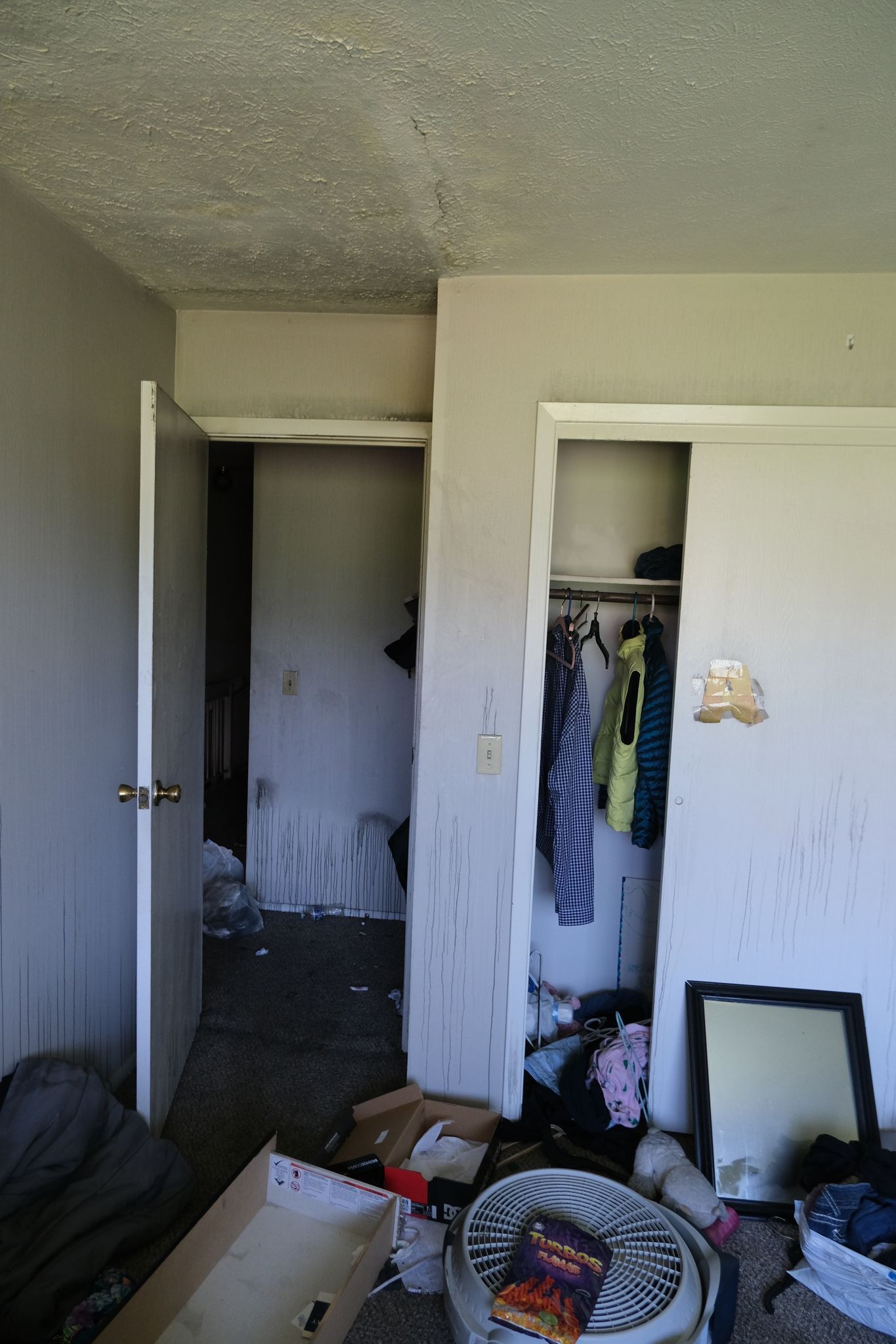 Messy room interior with open closet, clothes, debris, and a doorway to a darker area.