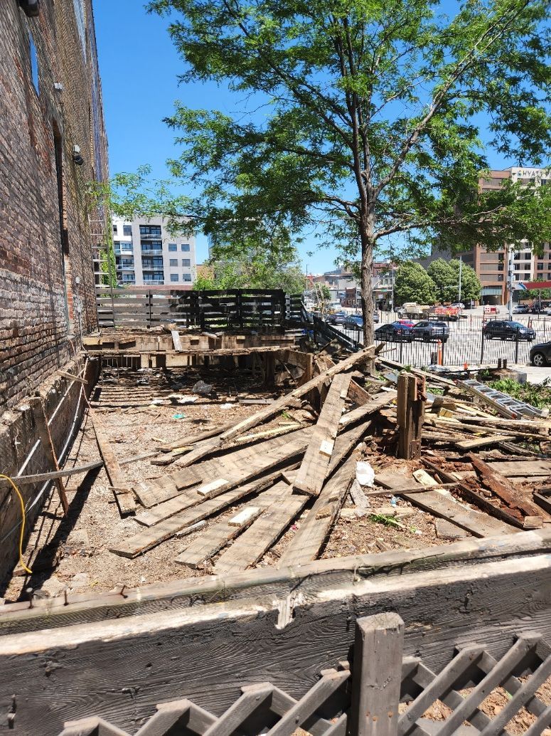 A pile of wood is sitting in front of a brick building.