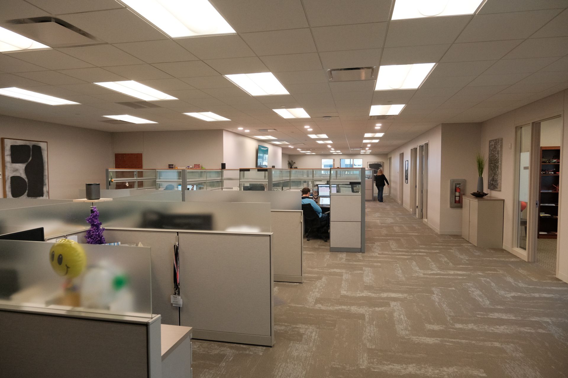 A large office with cubicles and a man walking down the hallway
