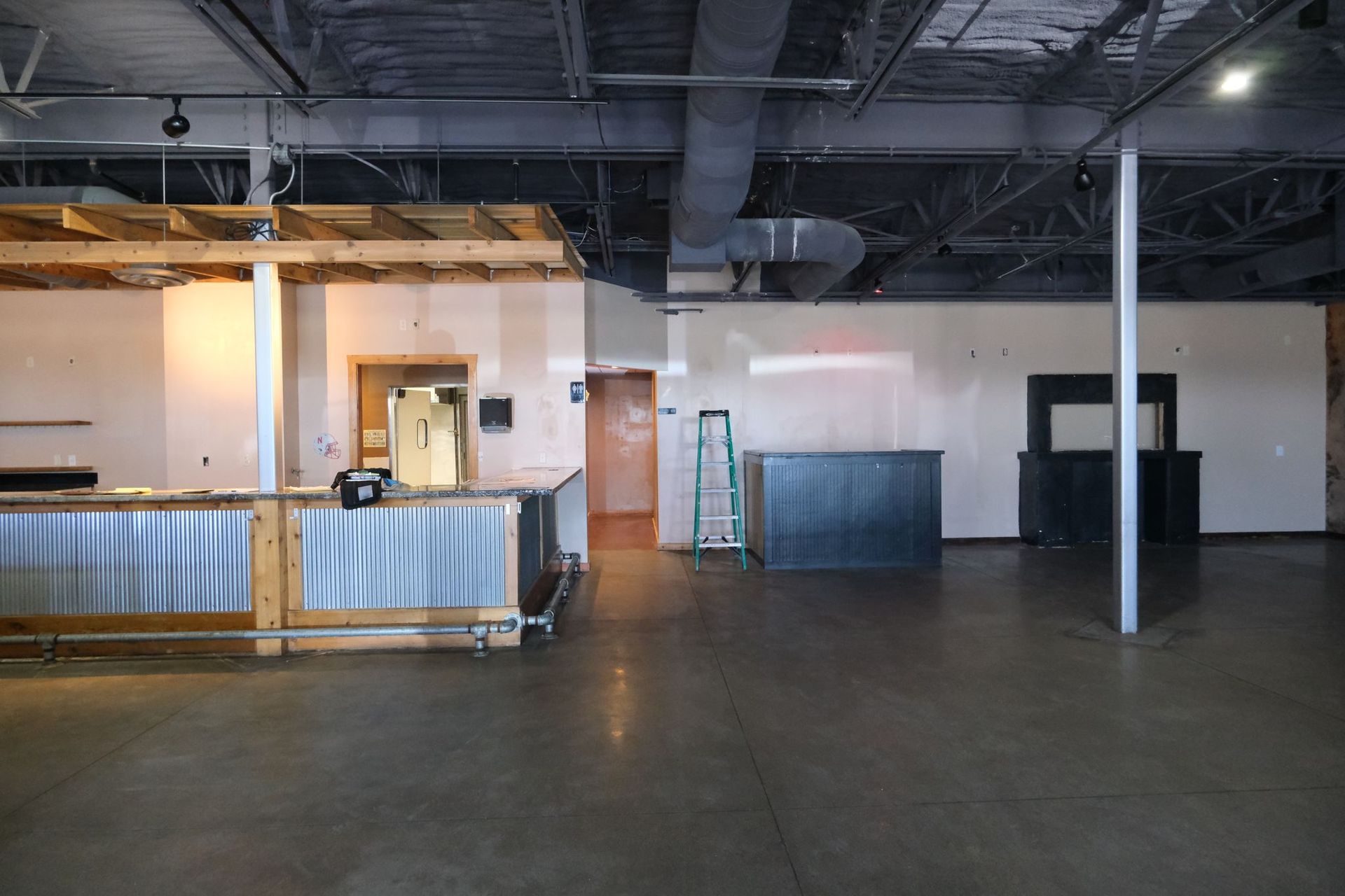 Empty commercial space with a bar, exposed ceiling, and concrete floor.