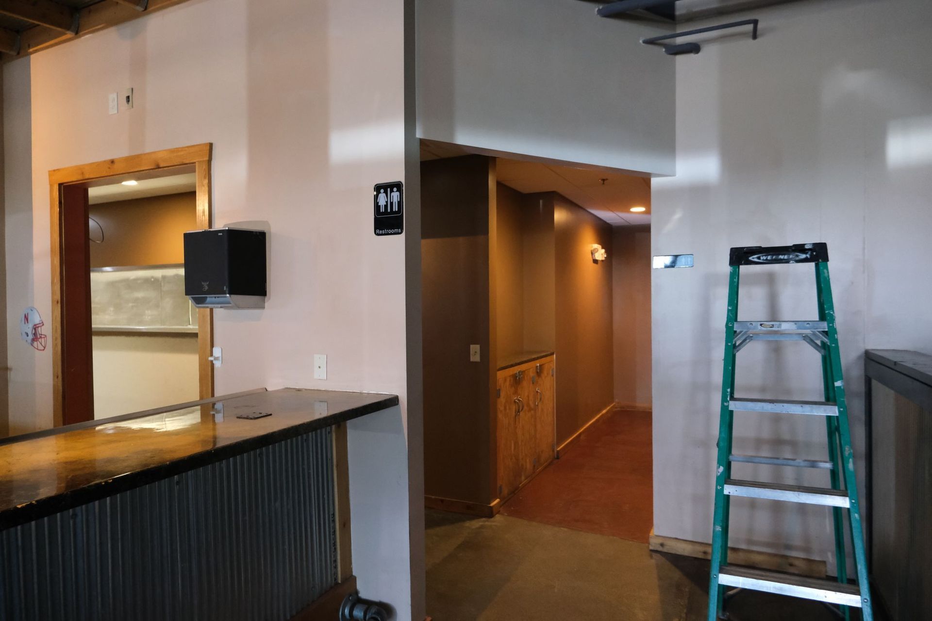 Interior of a bar with a hallway, restrooms, and a ladder.