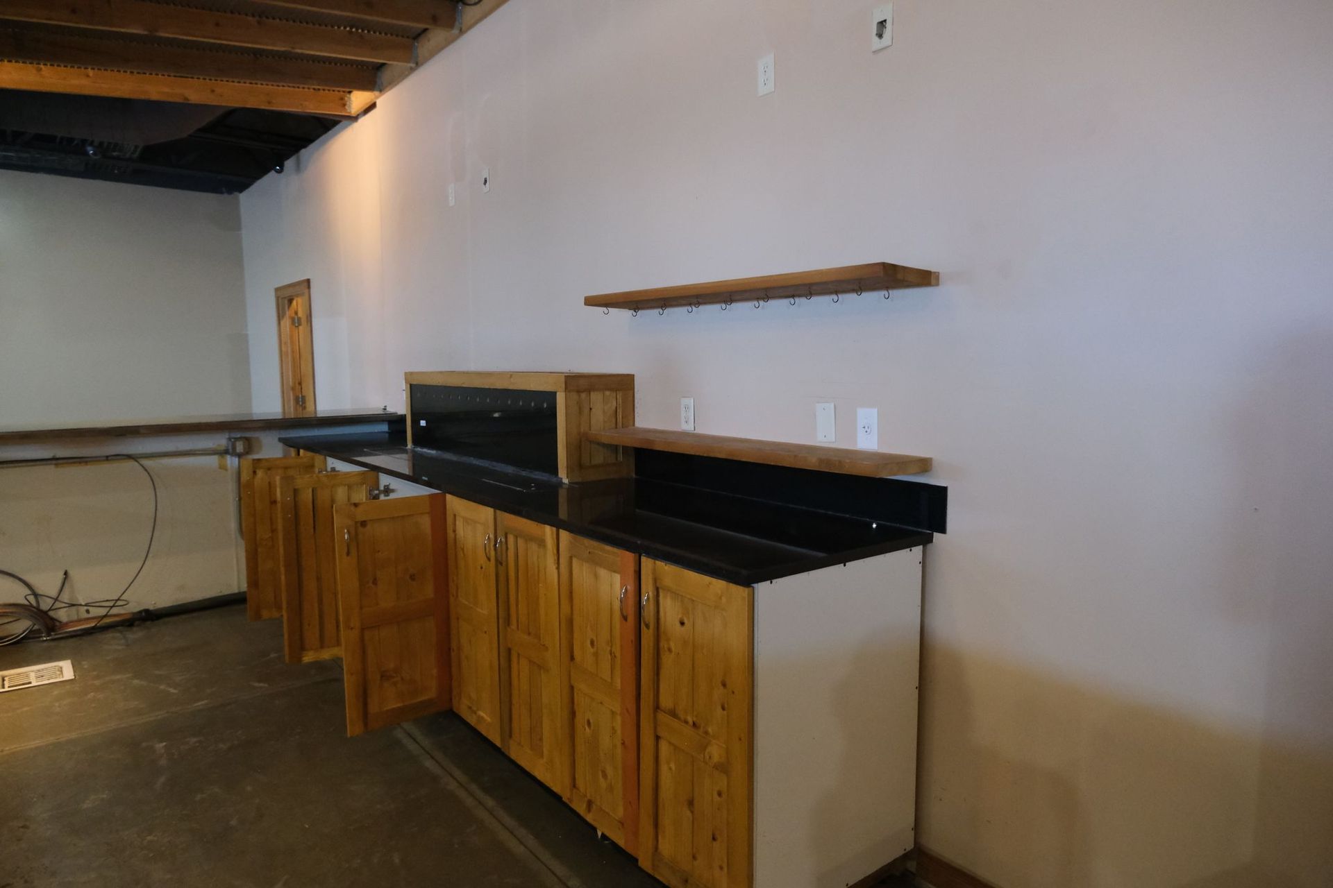 Kitchen cabinets with a black countertop and wooden shelves on a light gray wall.