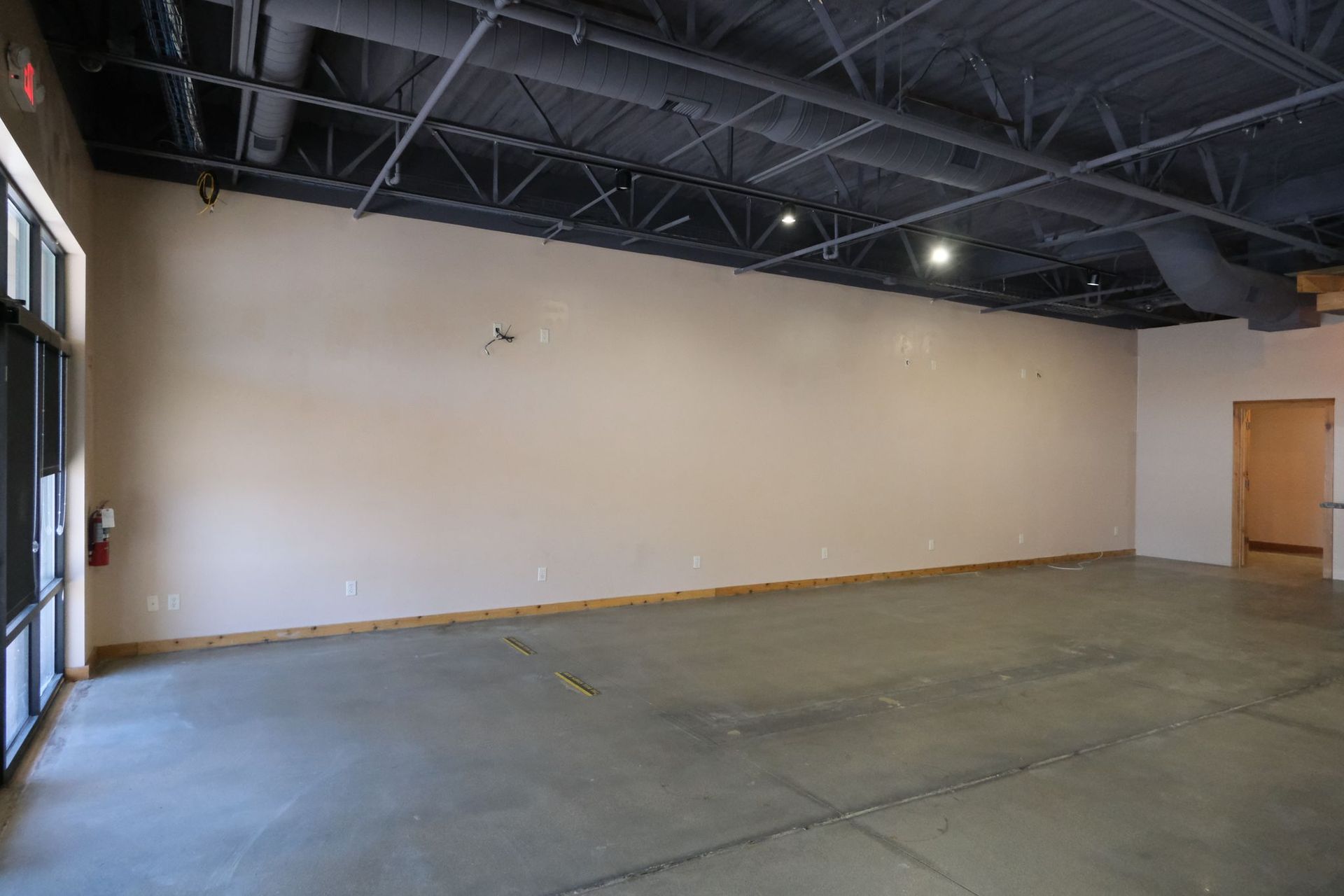 Empty commercial space with gray concrete floor, tan wall, and black ceiling.