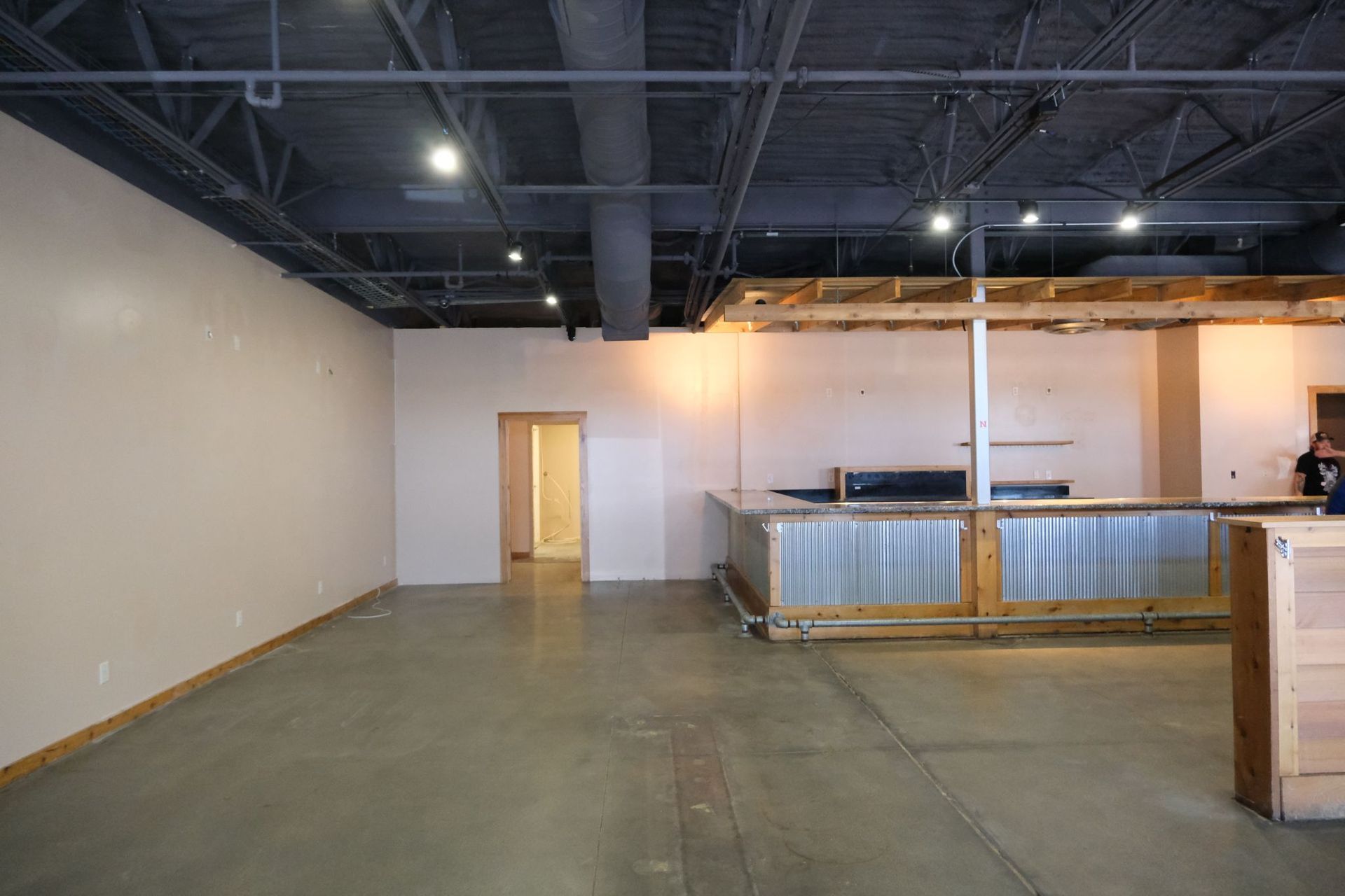 Empty commercial space with a bar, concrete floor, tan walls, and black ceiling.