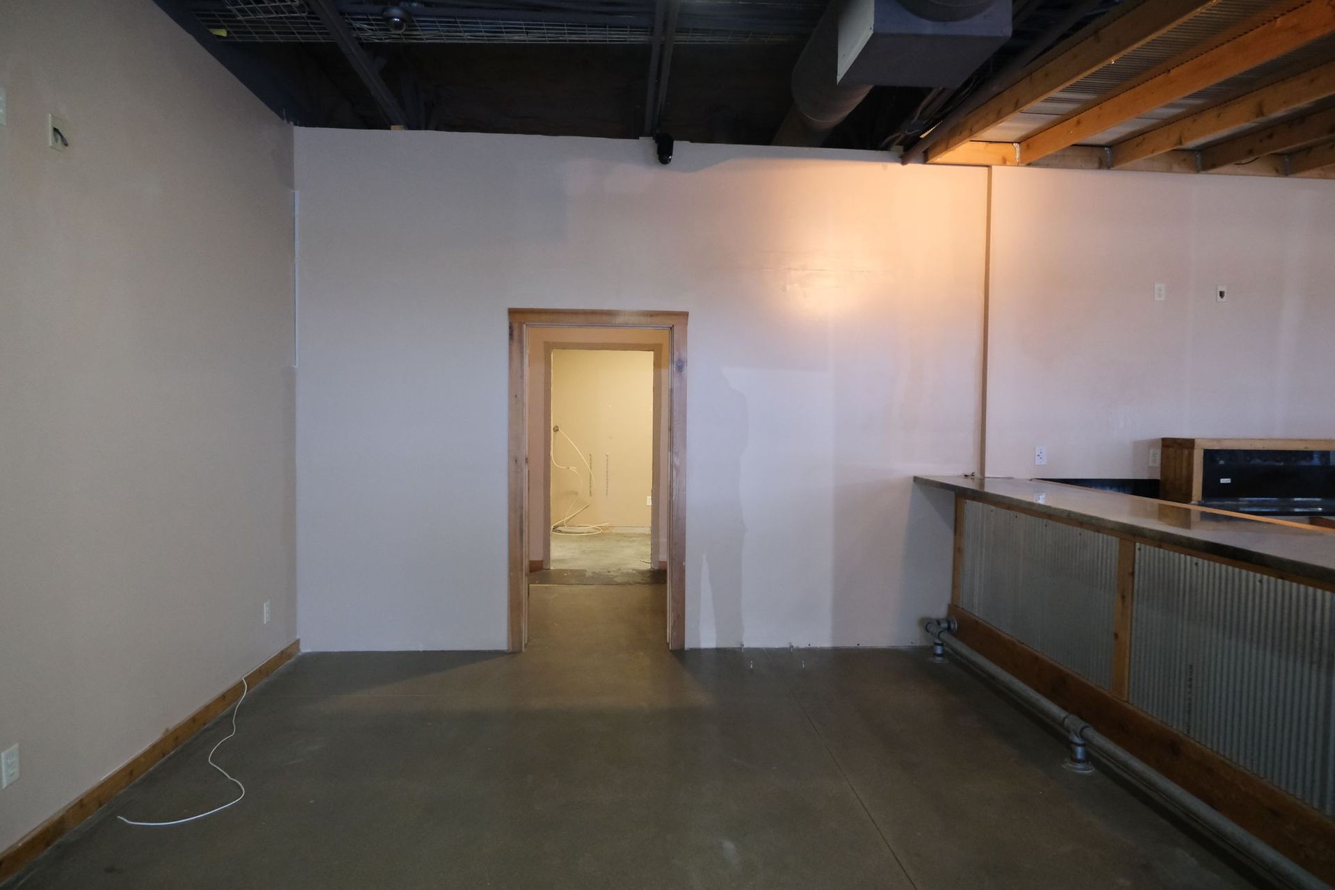 Empty commercial space with concrete floor, bar, door, and white walls.
