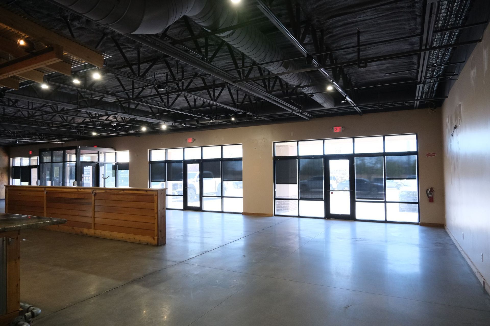 Empty commercial space with large windows and a wood-paneled wall.