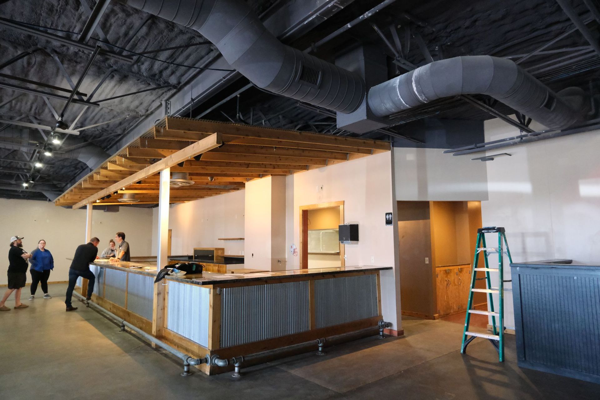 Bar under construction with corrugated metal, wooden features, and people.