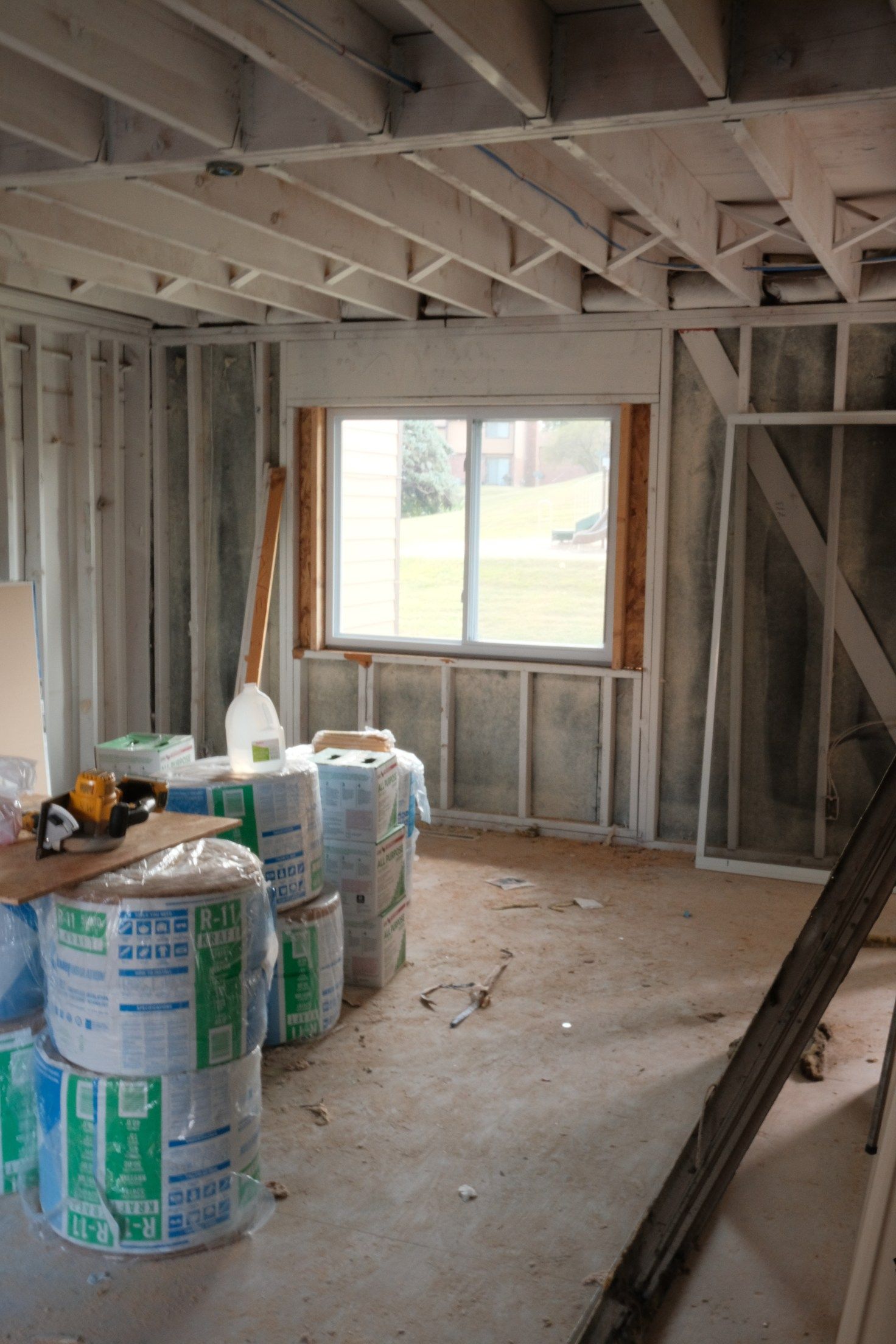 Interior of a room under construction. Insulation rolls stacked near a window, unfinished walls and ceiling.