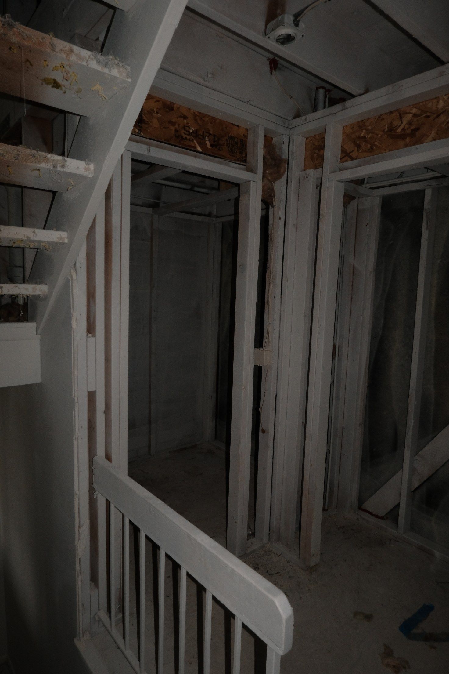 Interior view: unfinished room with stairs, doorway, and wooden frames. Painted white and gray.