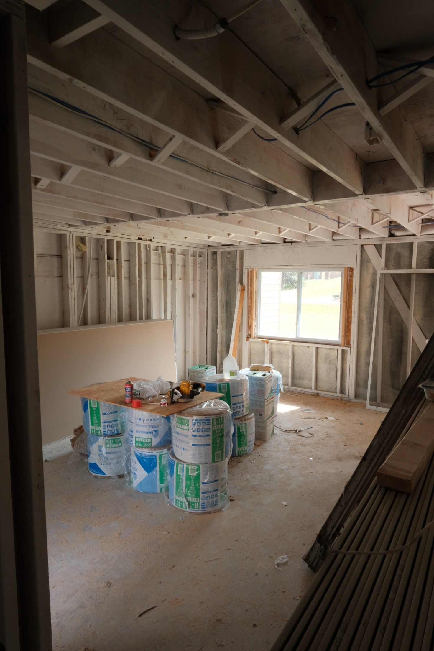 Interior view of a room under construction with exposed framing, insulation rolls, and a window.