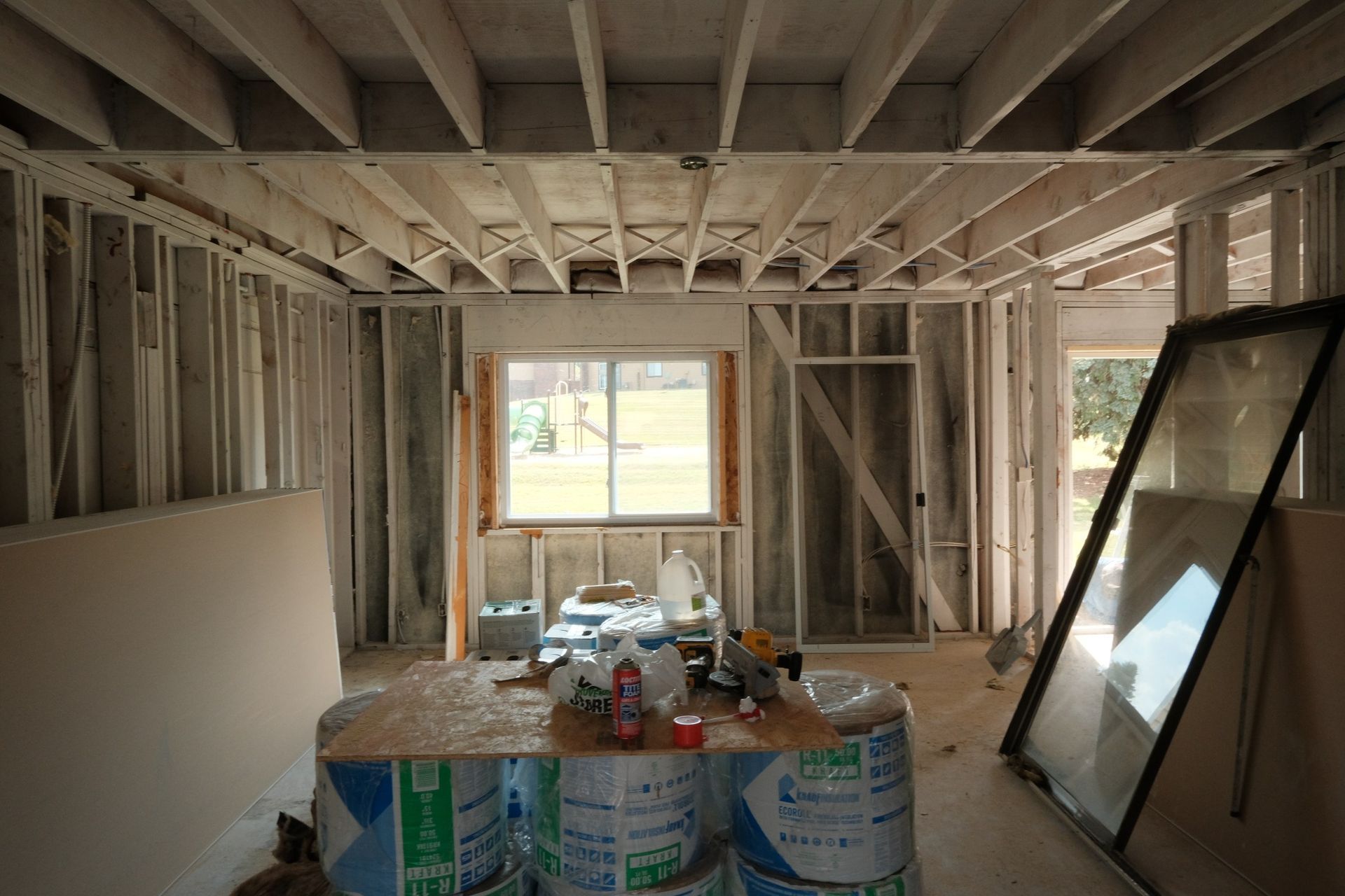 Interior of a room under construction with exposed wooden framing, a window, and insulation rolls.